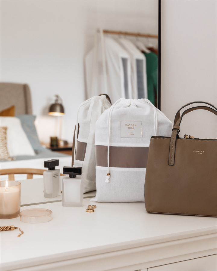 a Hayden Hill dust bag sitting next to a brown handbag on a dressing table