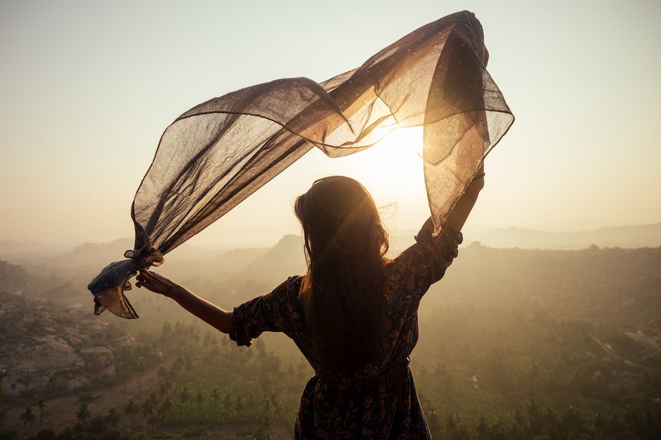 a woman standing on a hilltop at dusk  holding her chiffon scarf above her head
