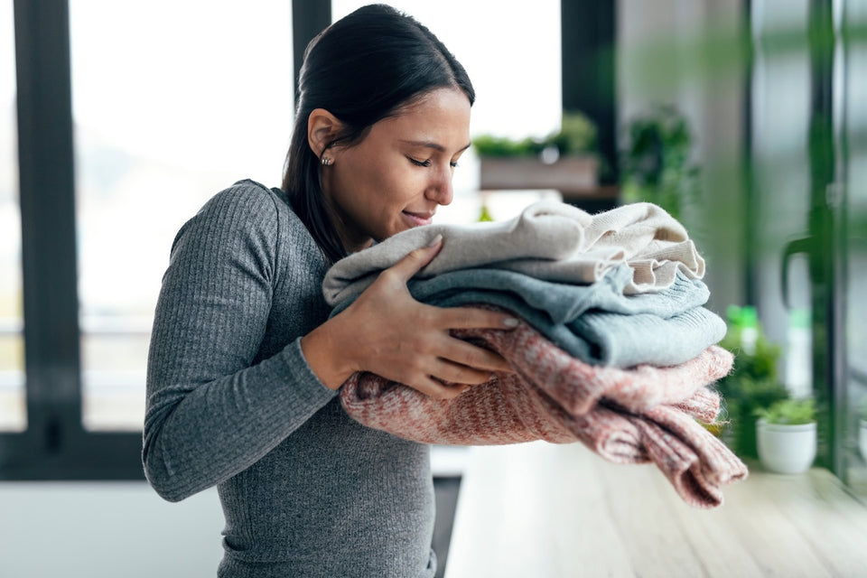a woman smelling a pile of freshly washed wool sweaters