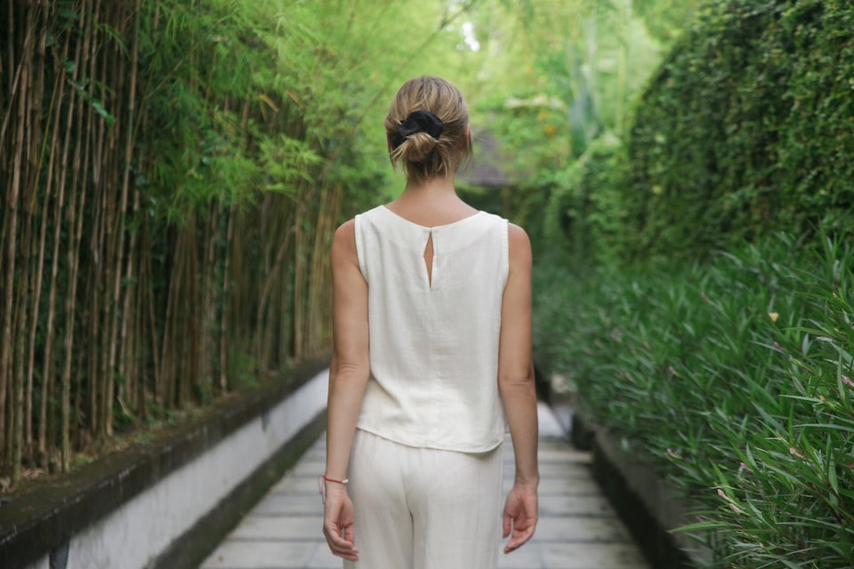 a woman standing with her back to the camera wearing a linen cream sleeveless top and matching linen trousers