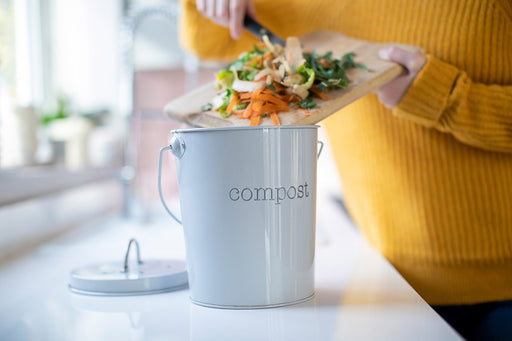 mixed vegetable scraps being put into a kitchen compost caddy