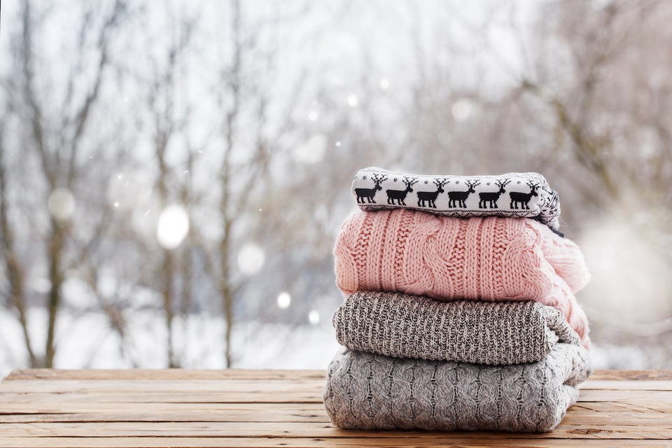 a pile of woollen sweaters sitting on a wooden table with a snowy winter background