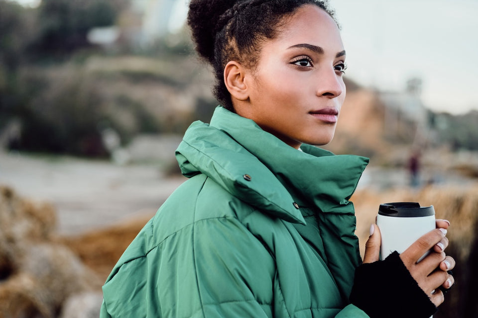 a woman wearing a green quilted jacket and holding a recyclable cup