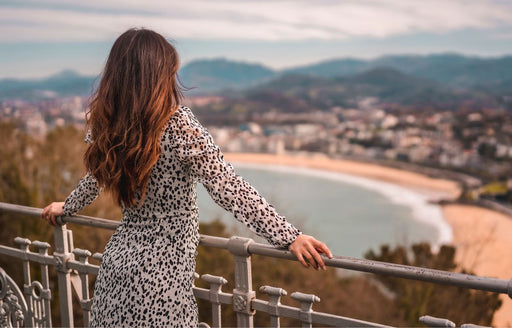 the back view of a woman admiring the view over a bay wearing a black and white patterned long sleeve dress