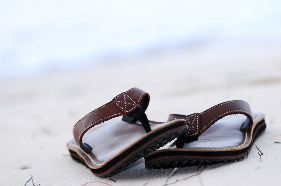 a close up of a pair of brown leather thong sandals on the beach